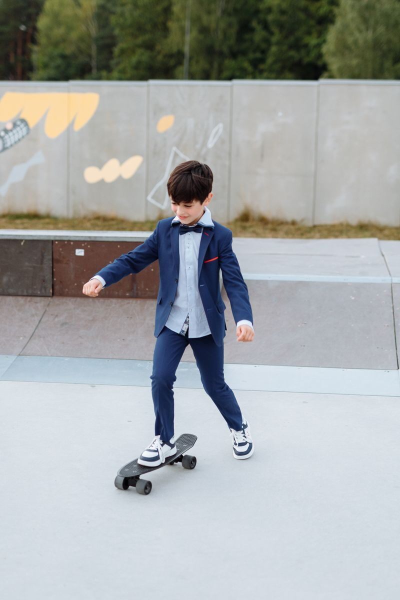 Young boy in a suit skateboarding in an outdoor skate park, enjoying leisure time.